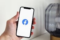 Close-up of a hand holding a smartphone displaying the Facebook logo indoors.